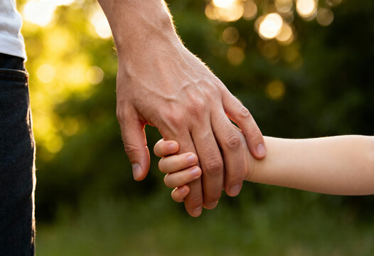 Close-up of a fathers hand holding a child's hand outdoors with a bright green background