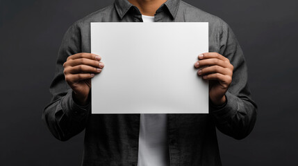 Naklejka premium Man Holding Blank White Paper Sheet on Dark Background – Mockup for Message or Design