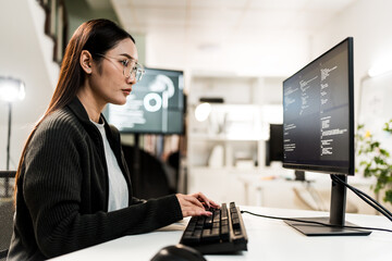 Focused female programmer coding on a computer in office. Young Asian software developer thinking and solving a problem. Women in tech concept