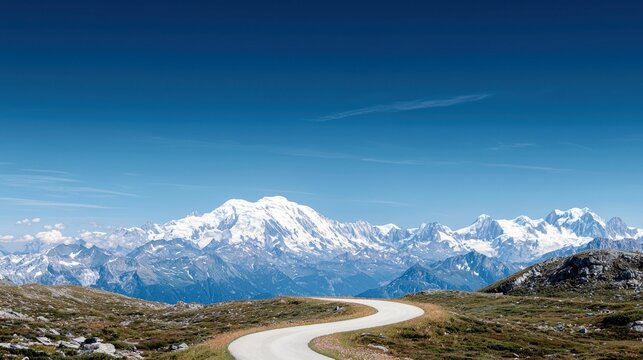 A scenic view of a winding road leading towards snow-capped mountains under a clear blue sky on a bright sunny day.