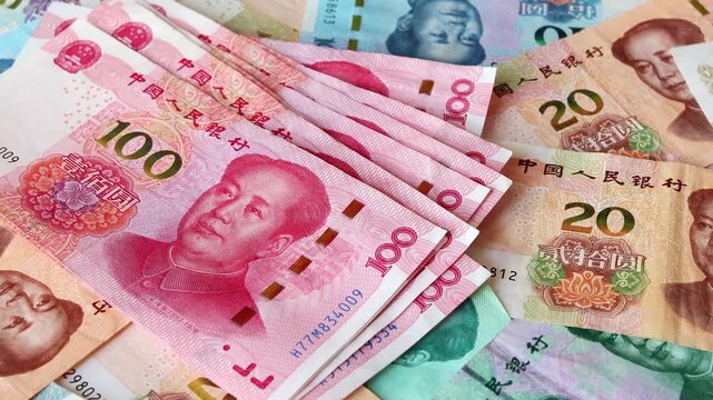 A wad of Chinese one hundred yuan (CNY) or renminbi (RMB) bills fall over table with heap of scattered notes of diffrent value. Saving money, financial income and growth, business concept.