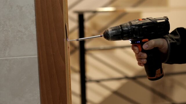 Side-angle view of cordless drill securing metal bracket on door frame