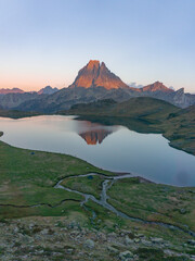 Mountain peak reflecting in lake with green grass and stream under a pastel sky at sunset or sunrise