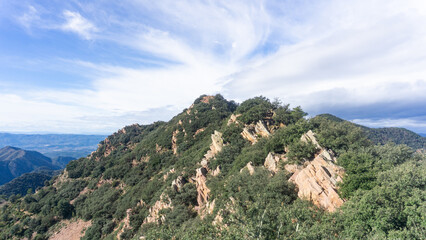View of a rocky mountain ridge covered in trees under a partly cloudy blue sky in a scenic landscape