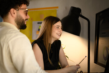 Business meeting in a modern office with a woman smiling while reviewing data on a computer screen with a male colleague during the afternoon