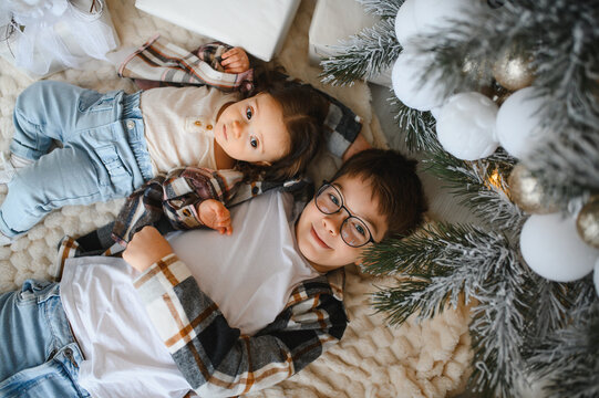 Cute siblings lying down cozy by christmas tree