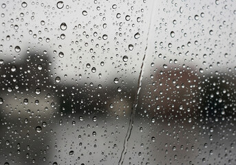 Raindrops clinging to a window pane, blurring the cityscape beyond, creating an abstract and atmospheric view on a gloomy, wet day outside