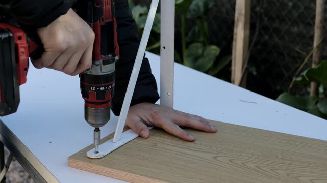 Battery-powered drill screwing metal bracket onto wooden panel edge