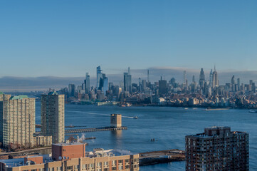 Obraz premium View from Jersey City showing clear sightlines toward the Manhattan skyline with bright daylight reflecting across the Hudson River and surrounding towers. 