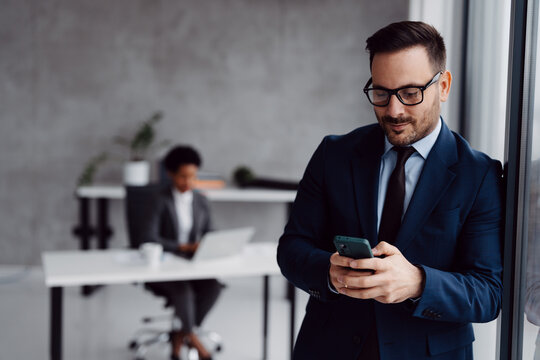 A businessman in a modern office standing near a window and using his smartphone
 - Powered by Adobe