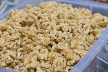 A macro detailed shot of a shelled walnuts kernels placed in a clear plastic bin. The kernels and are coated in a layer of sugar or honey sweet syrup, giving them a shiny, caramelized nuts