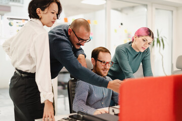 Fototapeta premium Team collaboration in a modern office with four businesspeople engaged in a project discussion around a computer in a bright workspace