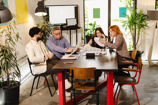 Meeting of creative professionals discussing project ideas in a modern office space with plants and technology around them