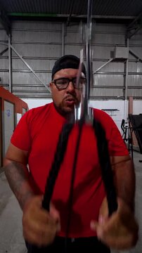 Video of a plus size man working out with a pulley machine at the gym. The scene captures real effort and focus during an authentic fitness routine in a casual indoor setting.