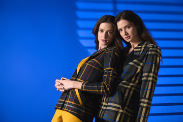 Stylish twin sisters showcase trendy outfits in vibrant blue setting