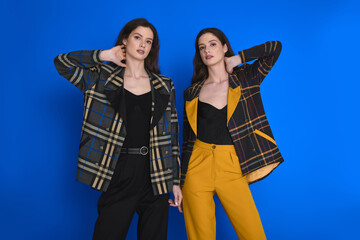 Stylish twin sisters showcase modern fashion against a vibrant blue background