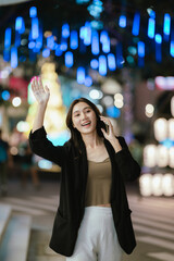 A smiling woman using her smartphone at night in a lively city setting, creating a warm and relaxed atmosphere with colorful blurred lights in the background.