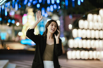 A smiling woman using her smartphone at night in a lively city setting, creating a warm and relaxed atmosphere with colorful blurred lights in the background.