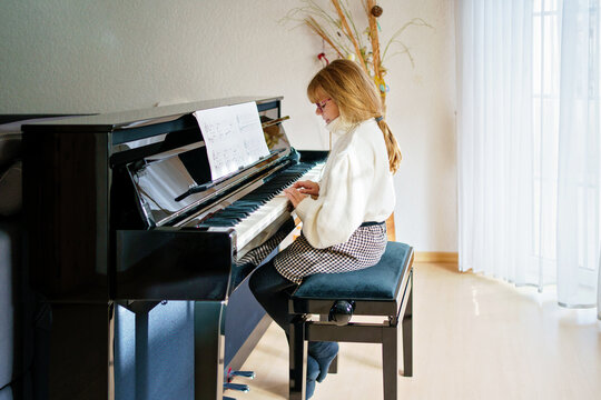 Little girl playing piano at home. Happy child practices music instrument