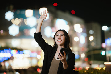 A smiling woman using her smartphone at night in a lively city setting, creating a warm and relaxed atmosphere with colorful blurred lights in the background.
