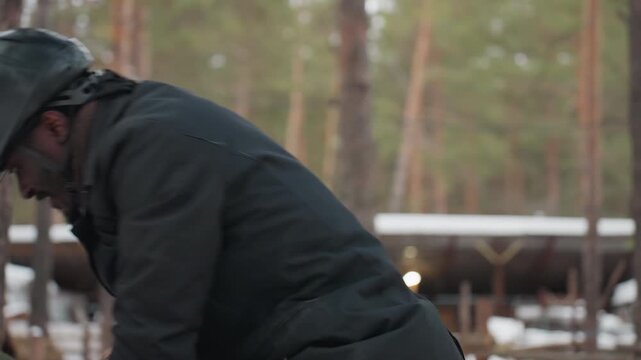 preparing equine for riding, man adjusting saddle straps outdoors, equestrian getting ready in snowy arena environment, individual securing horse tack outdoors with winter scenery in background