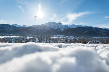 bright winter landscape featuring snow-covered ground, a small town, and distant mountain peaks under a clear blue sky. Sunlight creates a vivid, crisp atmosphere ideal. Holidays. Zakopane, Poland