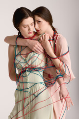 Twin sisters embrace each other in a creative fashion display with colorful threads