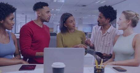 Discussing five colleagues leaning at desk in office in casual clothes, viewing tablet and laptop