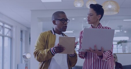 Comparing two coworkers holding tablet and laptop in office, in bomber jacket and striped shirt