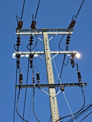 Close-up of a concrete utility pole with two cross arms holding multiple power lines, insulators,...