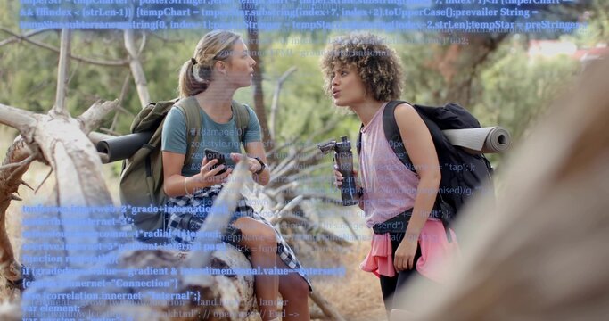 Sitting hiker talking, leaning pal holding tripod on log in forest with packs blue code overlay - Powered by Adobe