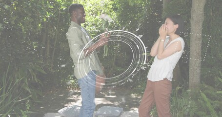 Presenting man in green shirt offering white bouquet in garden, woman covering mouth, overlay