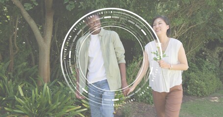 Walking couple wearing green shirt and white top holding sprig on park path, HUD overlay