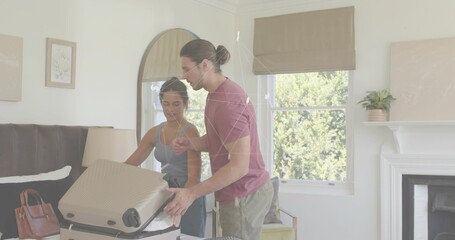 Packing couple leaning over beige hard-shell suitcase on bed in bedroom, handling leather handbag