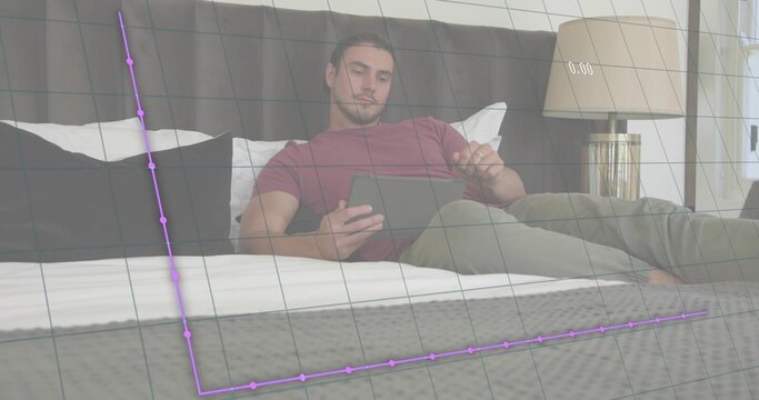 Reclining man in maroon tee and grey pants holding tablet on bed, viewing faint purple grid