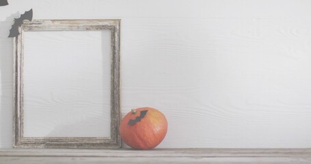 Fototapeta premium Displaying small orange pumpkin sitting on worn tabletop with frame and bat cutouts, copy space