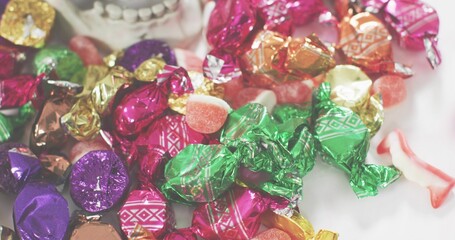 Glistening pile of assorted foil candies reflecting light on white tabletop, including gummy pieces