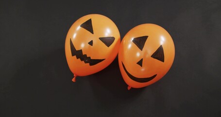 Fototapeta premium Displaying paired orange jack-o'-lantern balloons glowing under studio light, with knotted necks