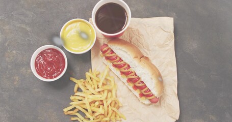 Displaying hot dog with mustard and ketchup on dark tabletop, with fries, dipping cups, copy space
