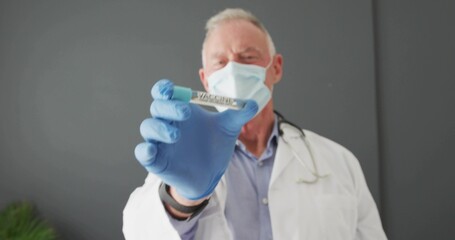 Holding senior doctor in lab coat, mask, blue gloves presenting vial in clinic, with stethoscope