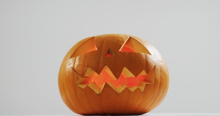Sitting carved pumpkin glowing with internal light on flat white surface against pale gray backdrop