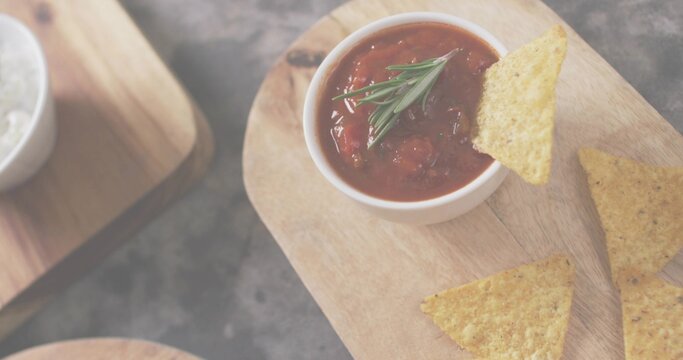 Fototapeta Showing white bowl of chunky tomato salsa with rosemary on wooden board, dark slate, nachos, salt