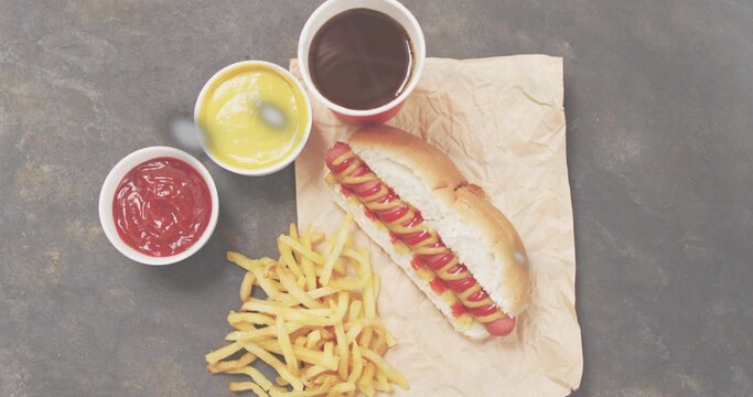 Fototapeta Displaying hot dog with mustard and ketchup on dark tabletop, with fries, dipping cups, copy space