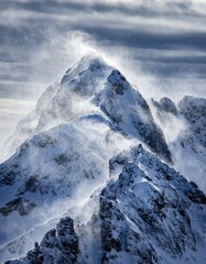 Obraz premium Majestic Snow-Capped Mountain Peak with Windy Conditions and Clouds