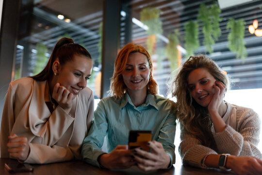 Three businesswomen engaged in a discussion over a smartphone at a modern workspace during a bright afternoon