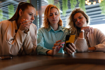 Businesswomen collaborating on a project at a modern cafe, discussing ideas while reviewing content on a smartphone in a vibrant and professional atmosphere
