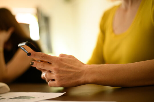 Young woman using smartphone while sitting at a table in a bright indoor space engaged with friends or coworkers