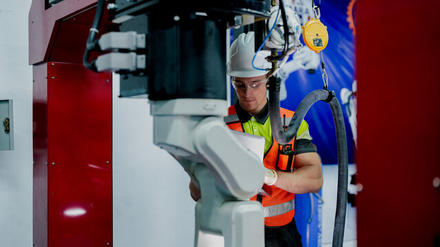 A robotics engineer uses a laptop to run diagnostics on an artificial intelligence robot. He is performing system maintenance in an advanced chip manufacturing lab.