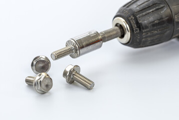 Close-up of a cordless drill with metal bit and three hex bolts resting on a white surface for hardware and DIY projects