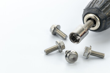 Close-up of a socket wrench attached to a drill surrounded by shiny steel bolts on a white surface